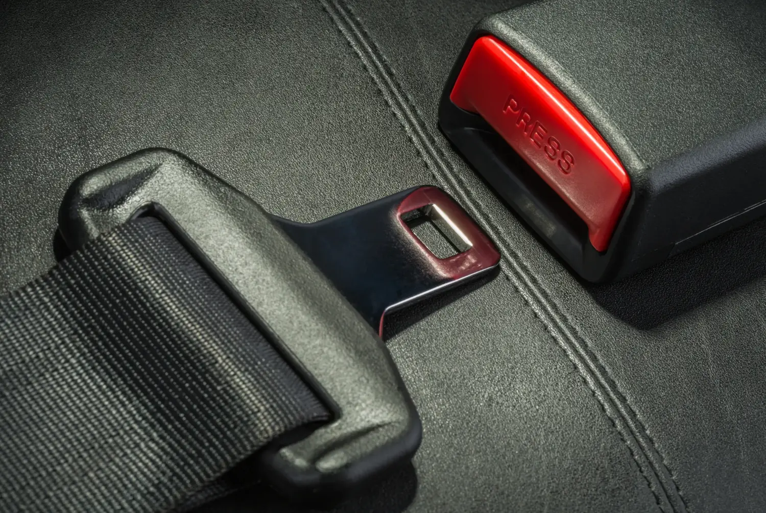 Seat belt buckle housing with a red release button positioned beside a latch plate on dark trim