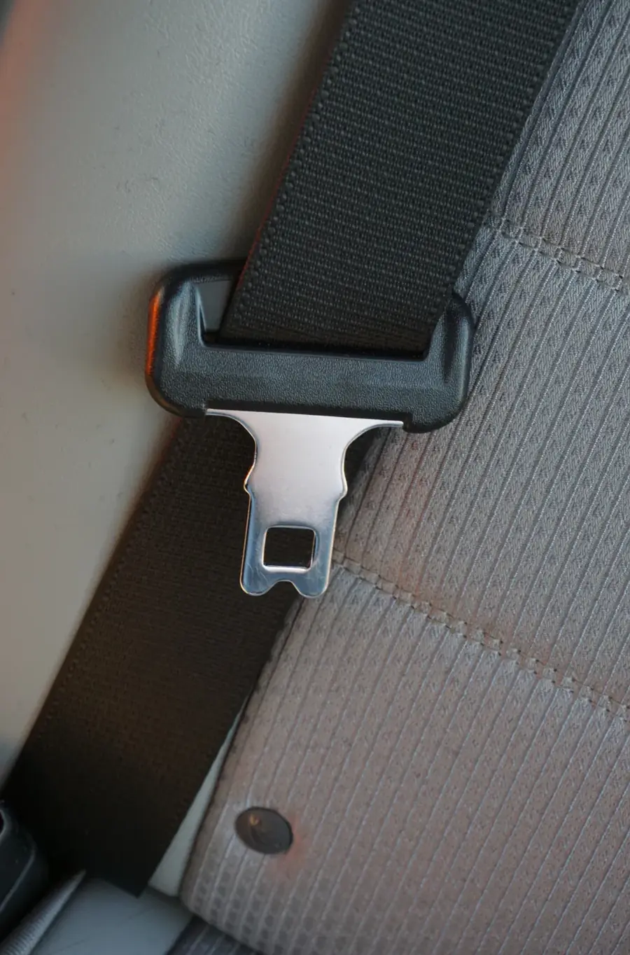 Seat belt webbing passing through a moulded upper guide with the metal tongue plate hanging below it