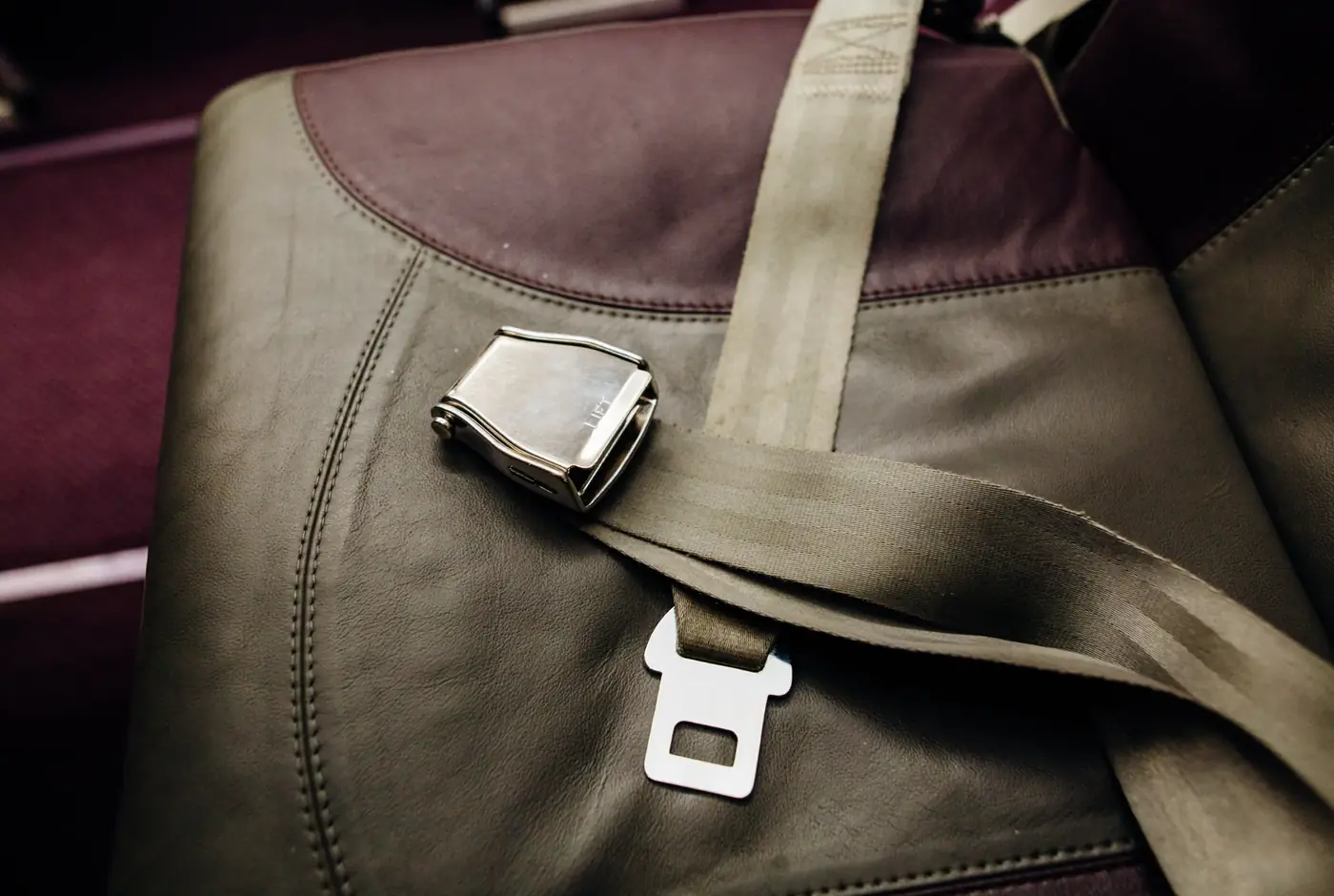Lap belt with a metal lift-latch buckle and webbing resting across an upholstered seat