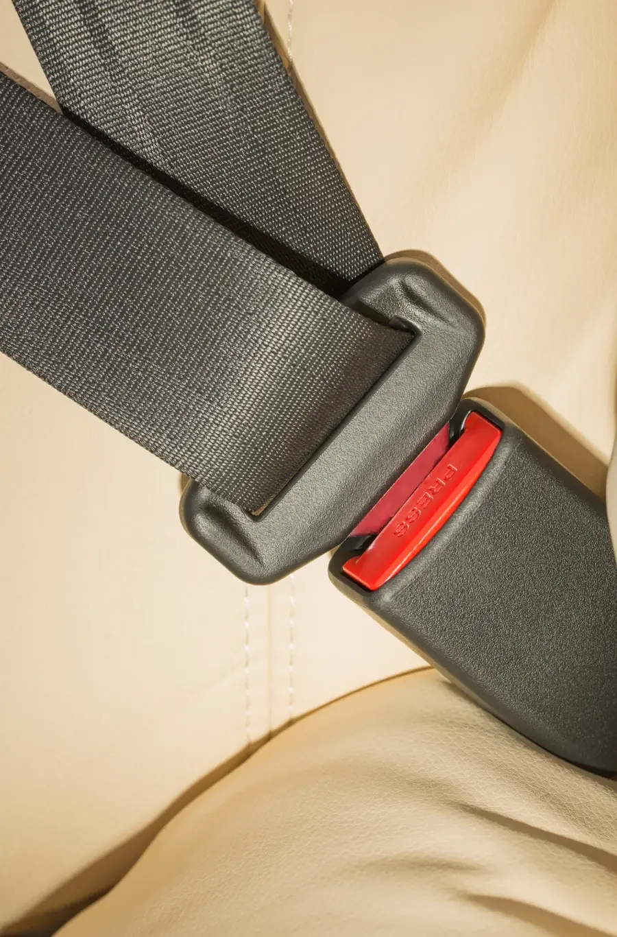 Seat belt webbing running down into a latched buckle across a light-coloured vehicle seat