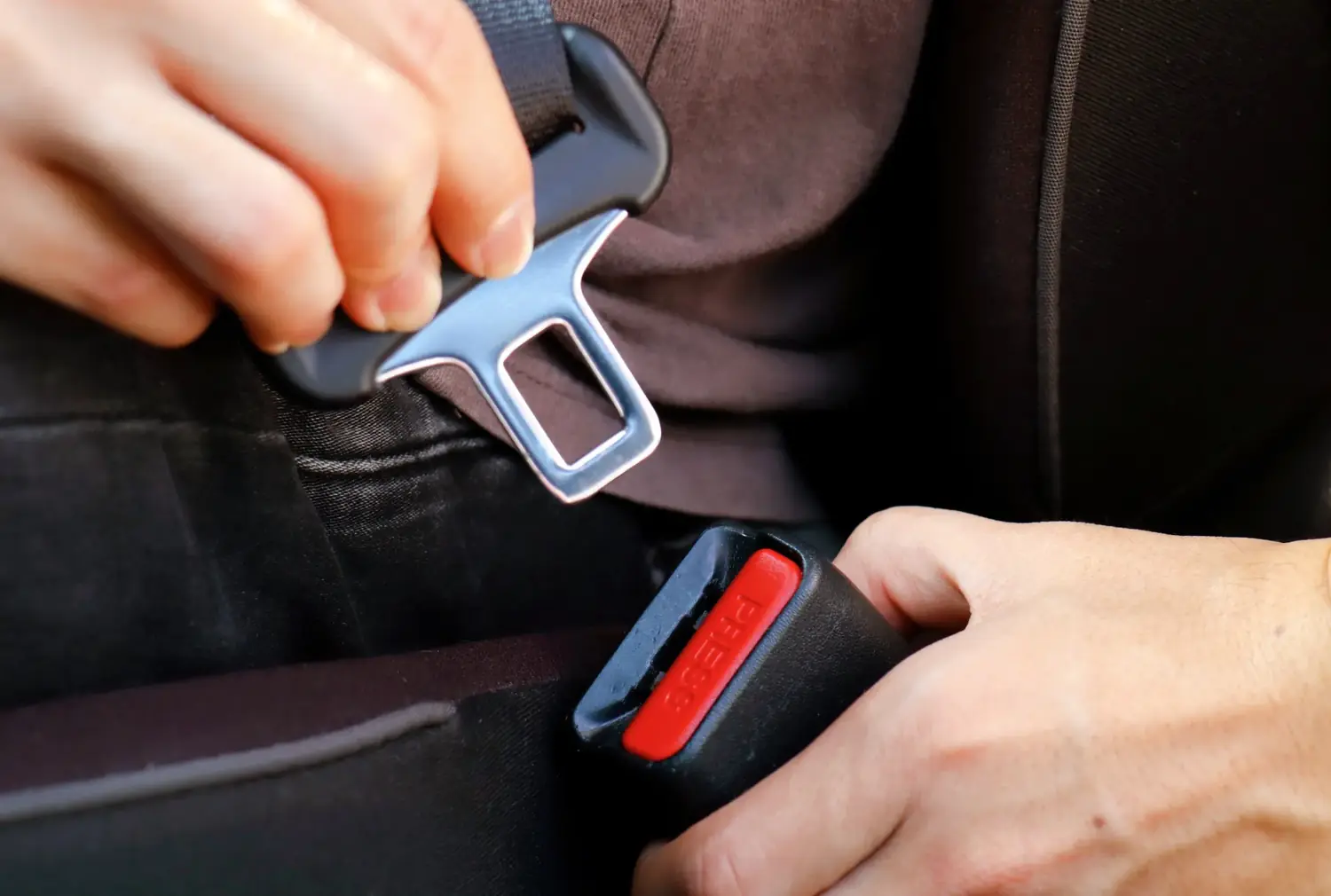 Hands guiding a seat belt tongue plate into the buckle housing to check engagement