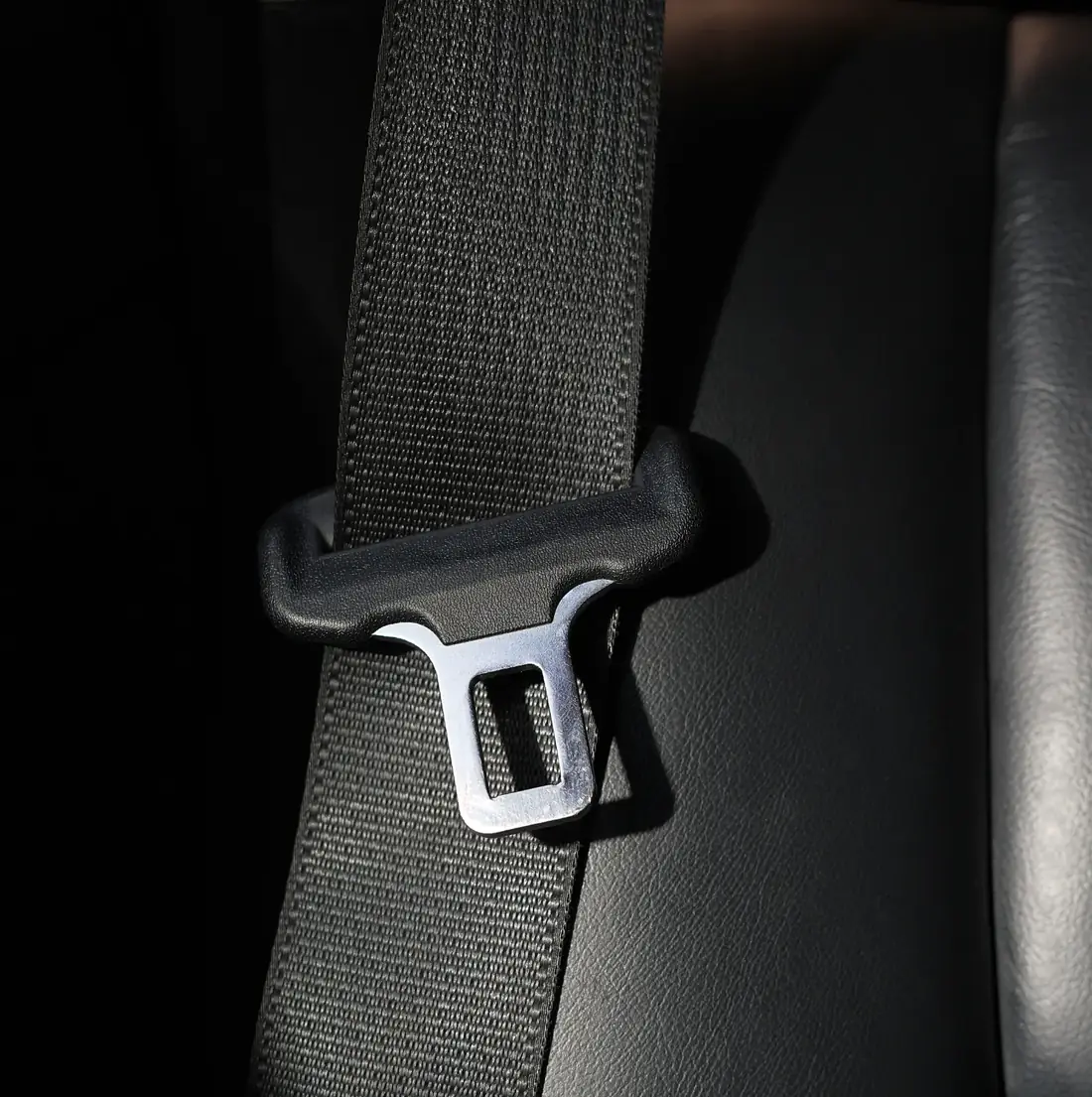 Seat belt webbing threaded through a moulded guide loop with the metal tongue plate alongside